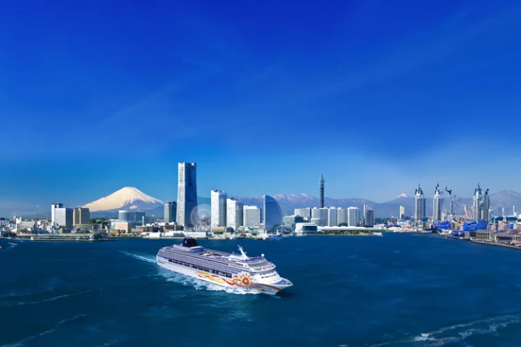 Gemini hat gesagt Ein großes Kreuzfahrtschiff mit bunter Bemalung fährt durch den Hafen von Yokohama, im Hintergrund ist der schneebedeckte Berg Fuji zu sehen.